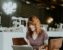 woman sitting on brown wooden chair while using silver laptop computer in room
